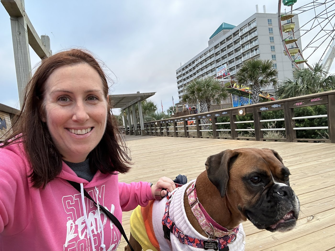Courtney on a beach boardwalk with her boxer in a sweater